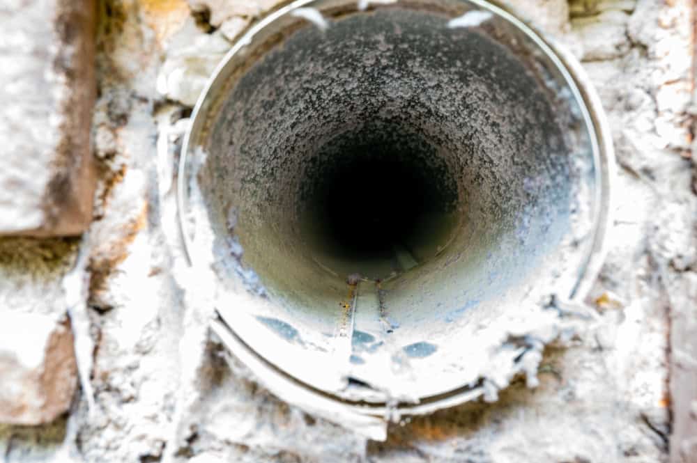 Close-up view of a narrow, cylindrical tunnel or pipe, reminiscent of those needing chimney repair in Fairfield County CT. Surrounded by a rough, textured surface with visible signs of wear and weathering, the interior extends into shadow.