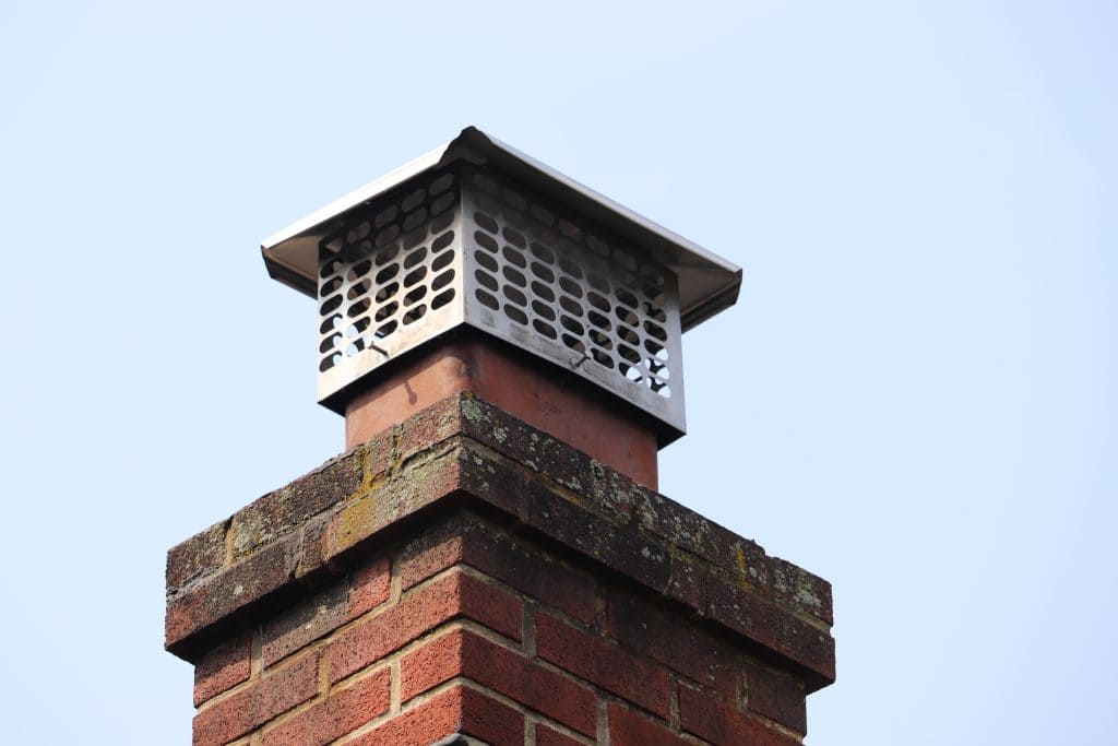 Close-up of a brick chimney with a metal cap from Chimney Caps Fairfield County CT. The grid design stands proudly against a clear blue sky, showcasing expert craftsmanship.